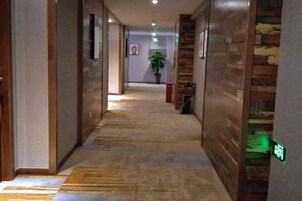 Un pasillo de hotel con piso alfombrado, paneles de madera y una señal de salida verde.