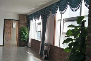 A hallway with a brick wall, a potted plant, and a window with blue curtains.
