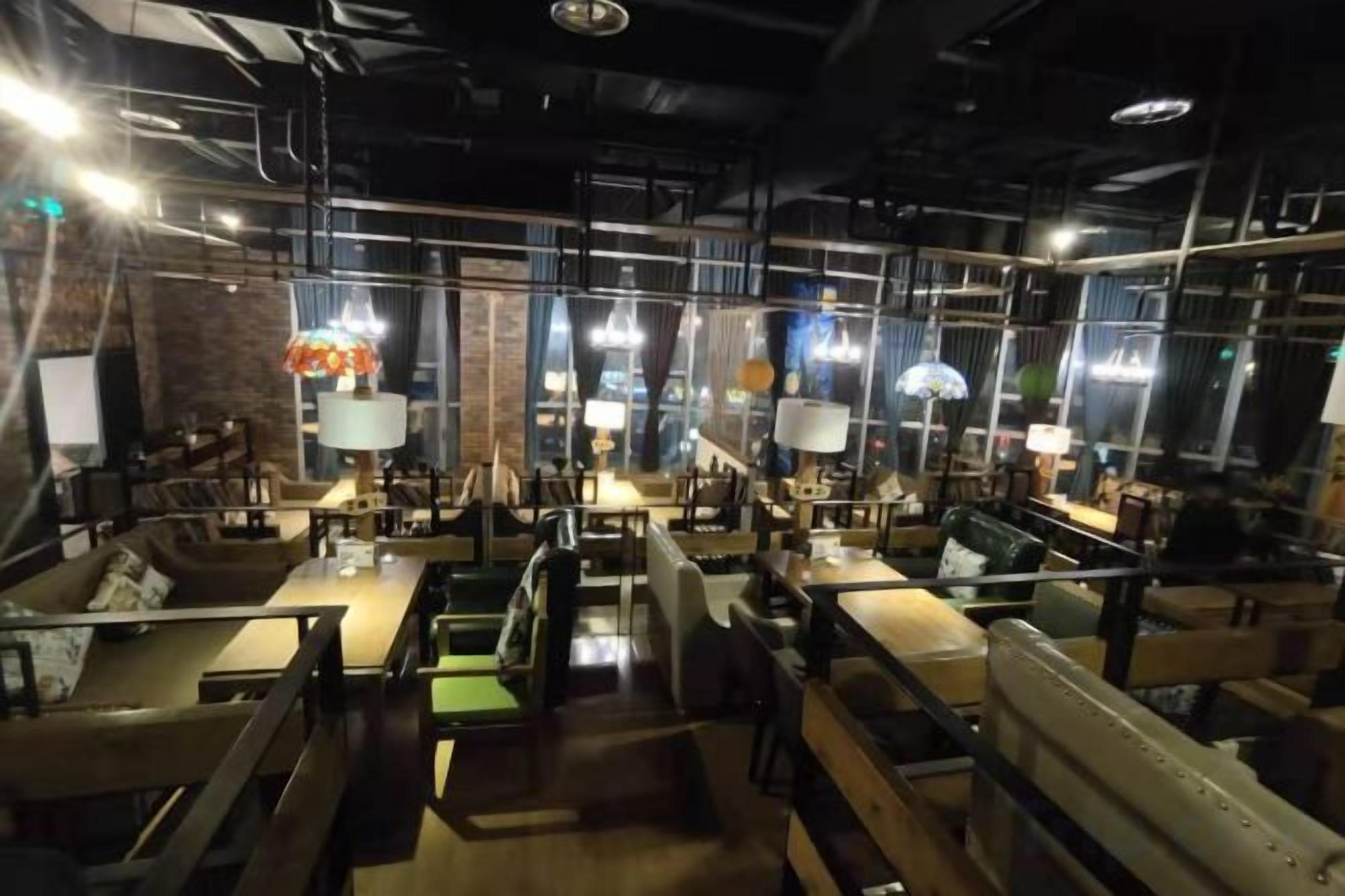 An indoor dining area with tables and chairs, overhead lighting, and a brick wall.