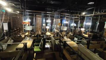 An indoor dining area with tables and chairs, overhead lighting, and a brick wall.