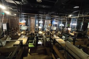 An indoor dining area with tables and chairs, overhead lighting, and a brick wall. - Renshou Wanye Sunshine Hotel (Renshou)