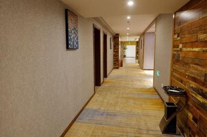 A hotel corridor with carpeted flooring, wooden panel walls, and doors leading to rooms.