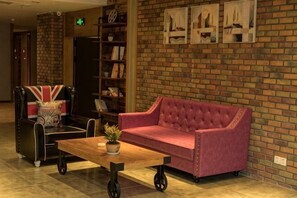A room with a red sofa, a black leather chair, a wooden coffee table, and a bookshelf against a brick wall.