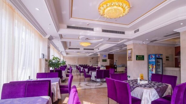 Un comedor de hotel con sillas y mesas moradas, un candelabro y una máquina expendedora de Pepsi.