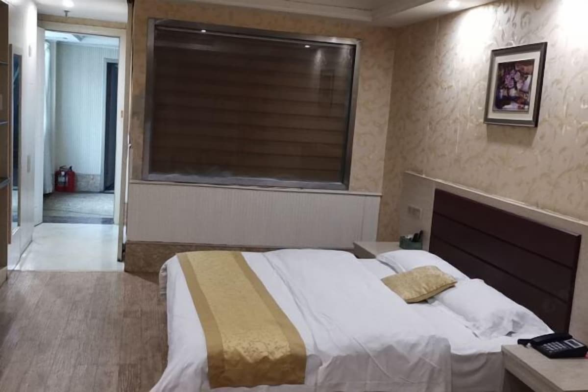 A hotel room with a bed, bedside table, and a window with blinds.