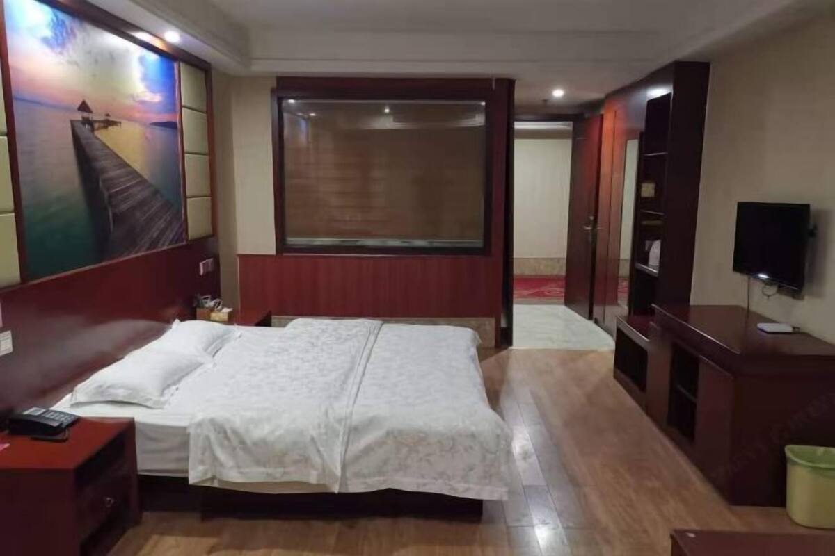 A hotel room with a bed, a desk, a TV, and a painting on the wall.