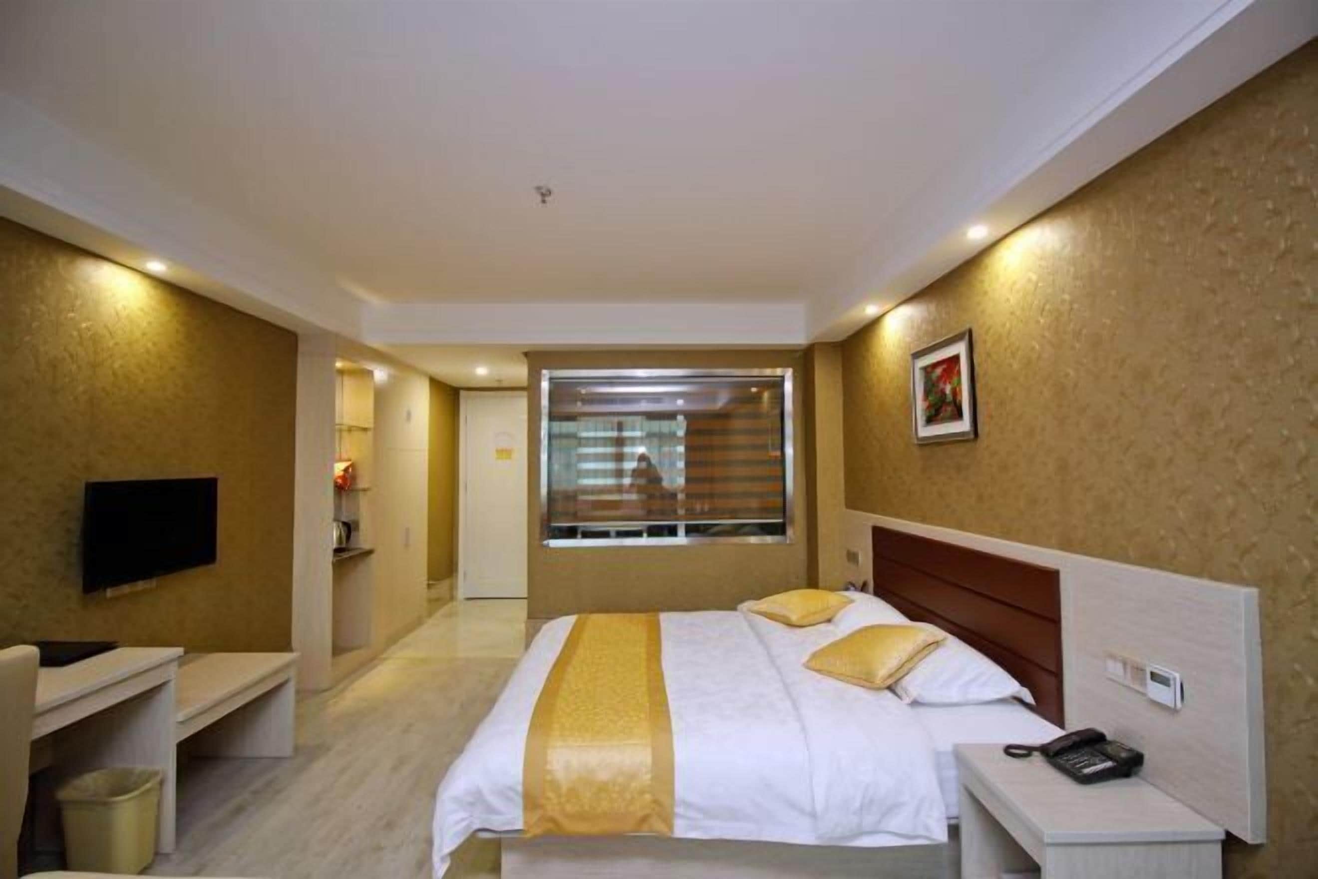 A hotel room with a bed, bedside table, and a TV mounted on the wall.