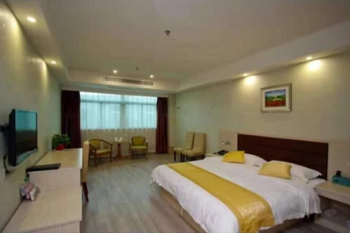 A hotel room with a bed, a desk, a chair, a TV, and a window.
