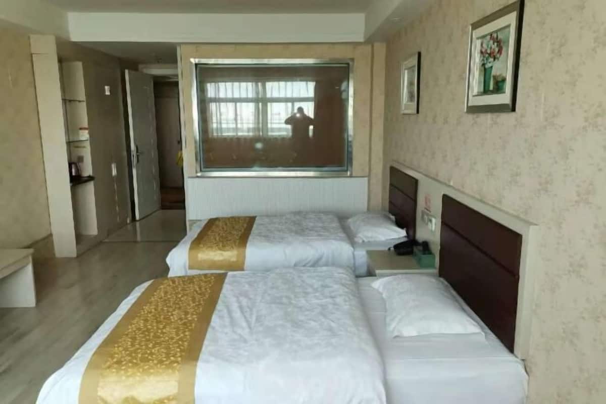 A hotel room with two beds, a large window, a mirror, and a framed picture on the wall.