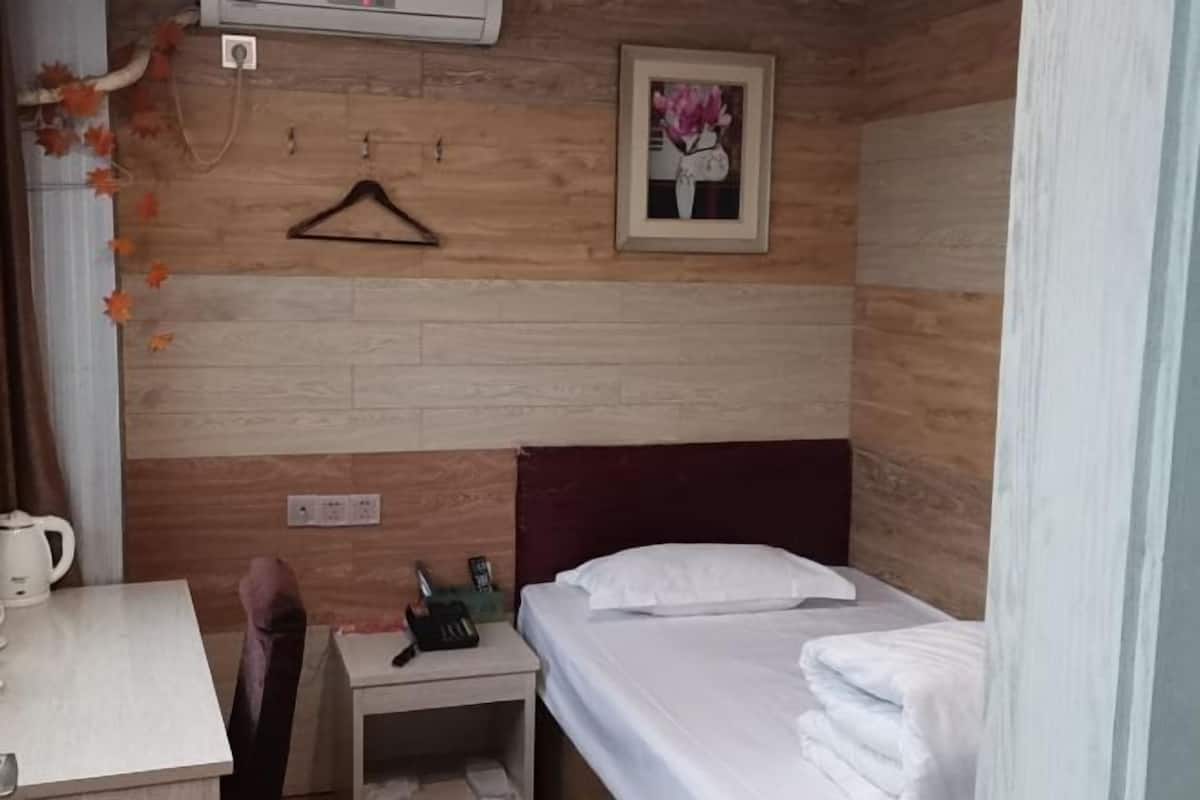 A room with a bed, a small table, a chair, a bedside table with a phone, and a picture on the wall.