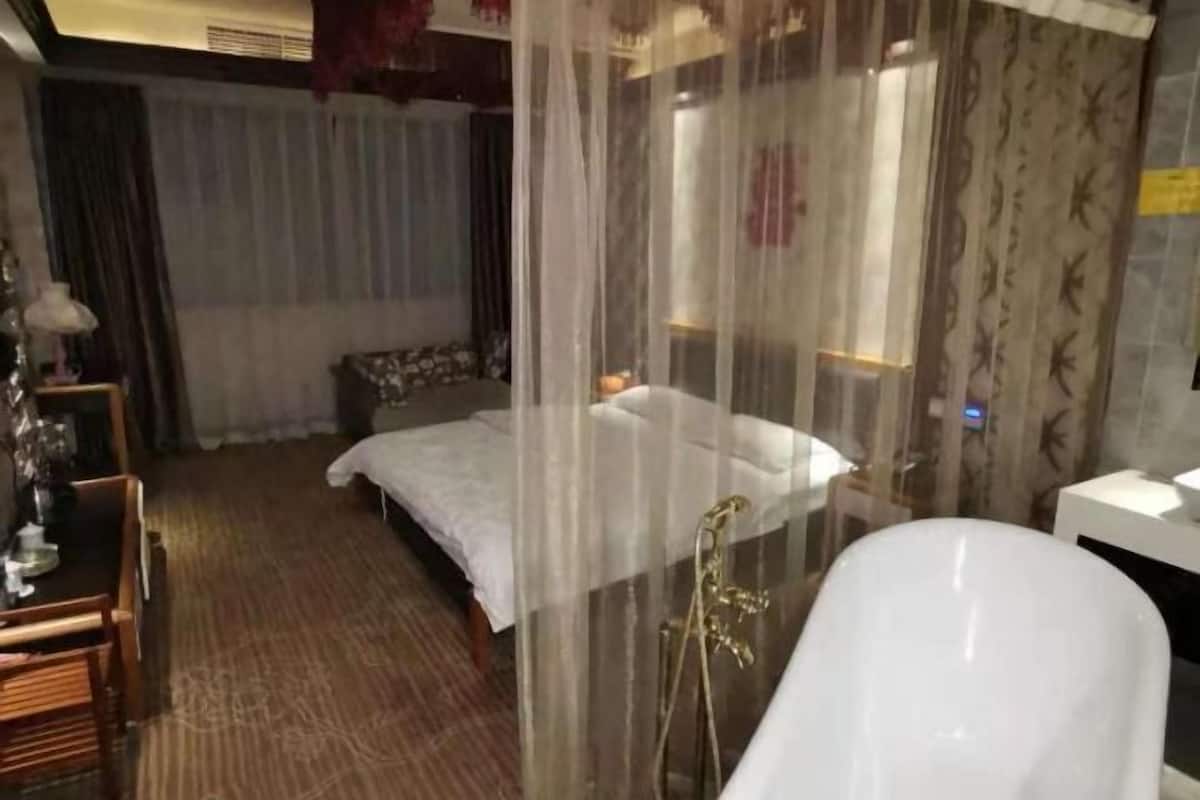 A hotel room with a bed, a shower area, a bedside table, and a chair.