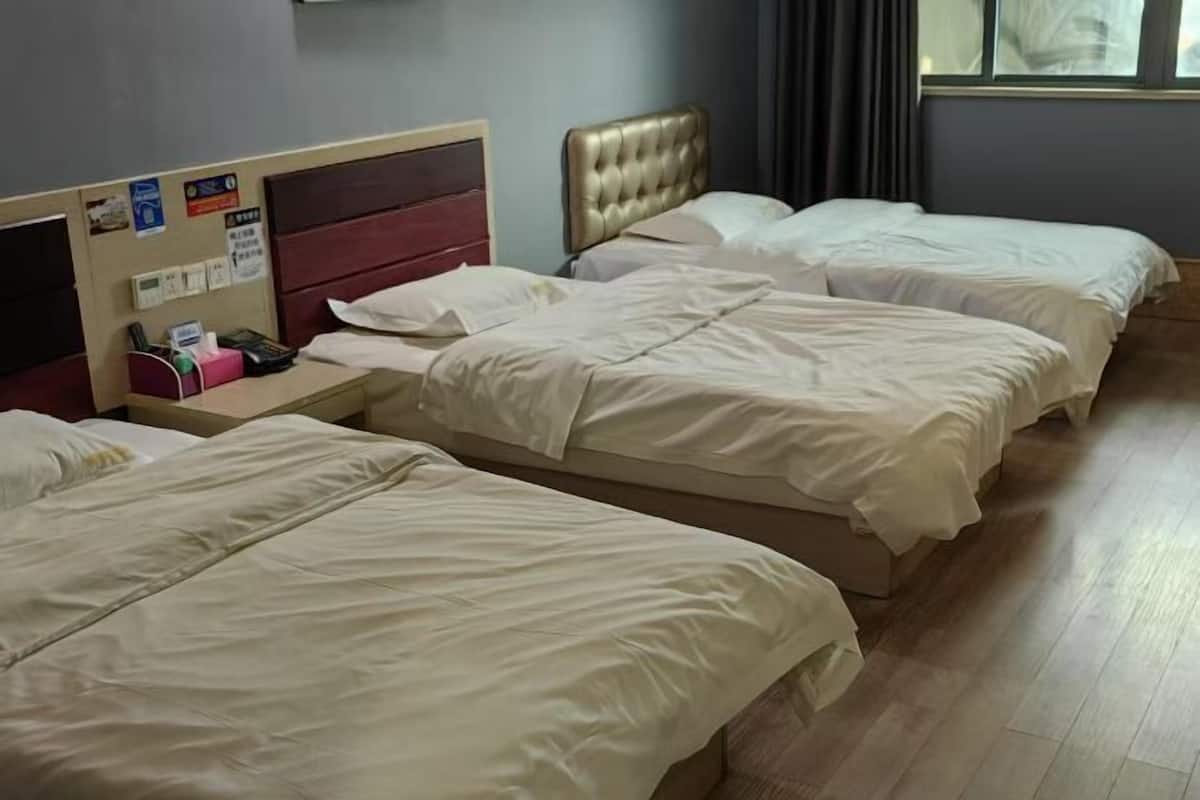A hotel room with three beds, a wooden floor, a wall-mounted phone, and a window with curtains.