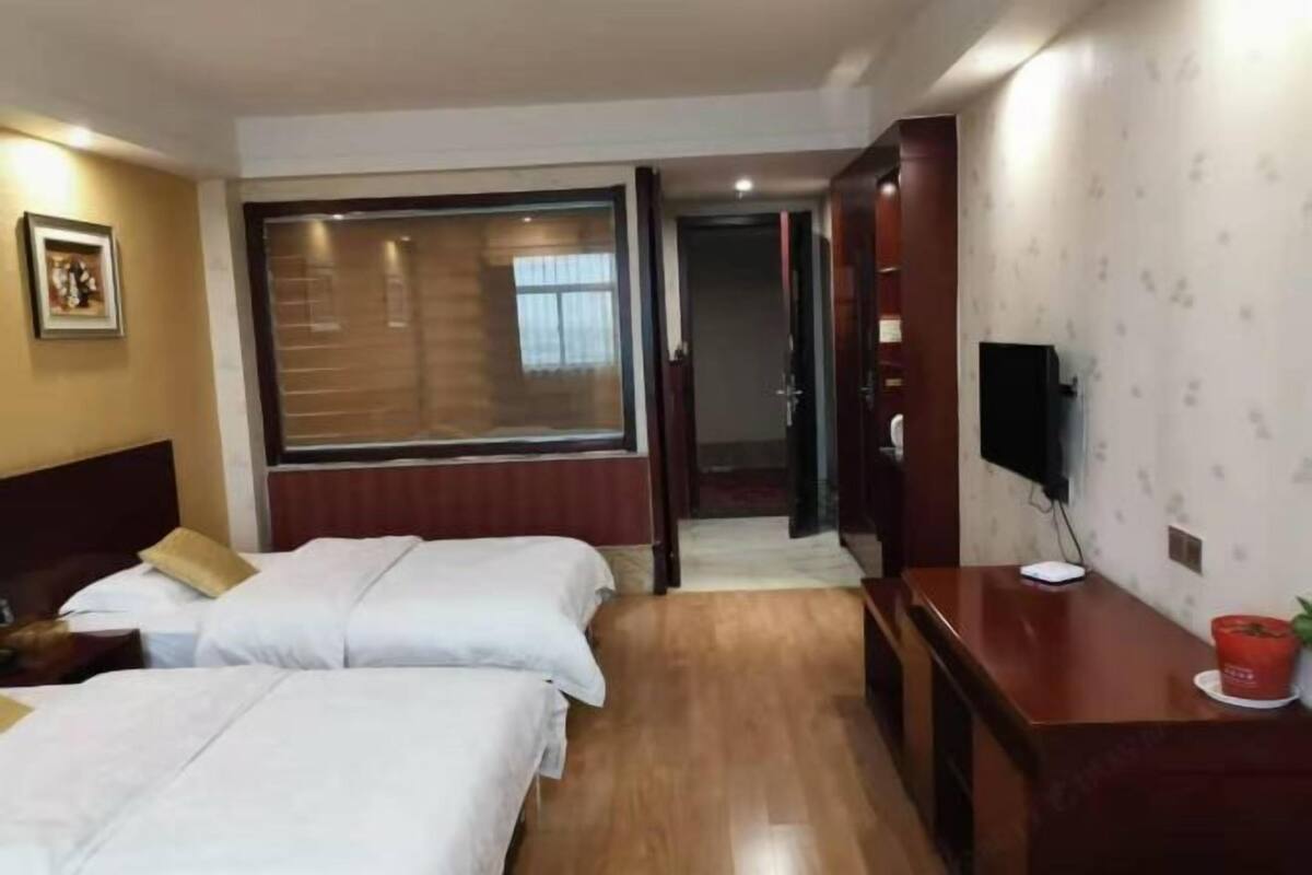A hotel room with two beds, a desk, a TV, and a window.