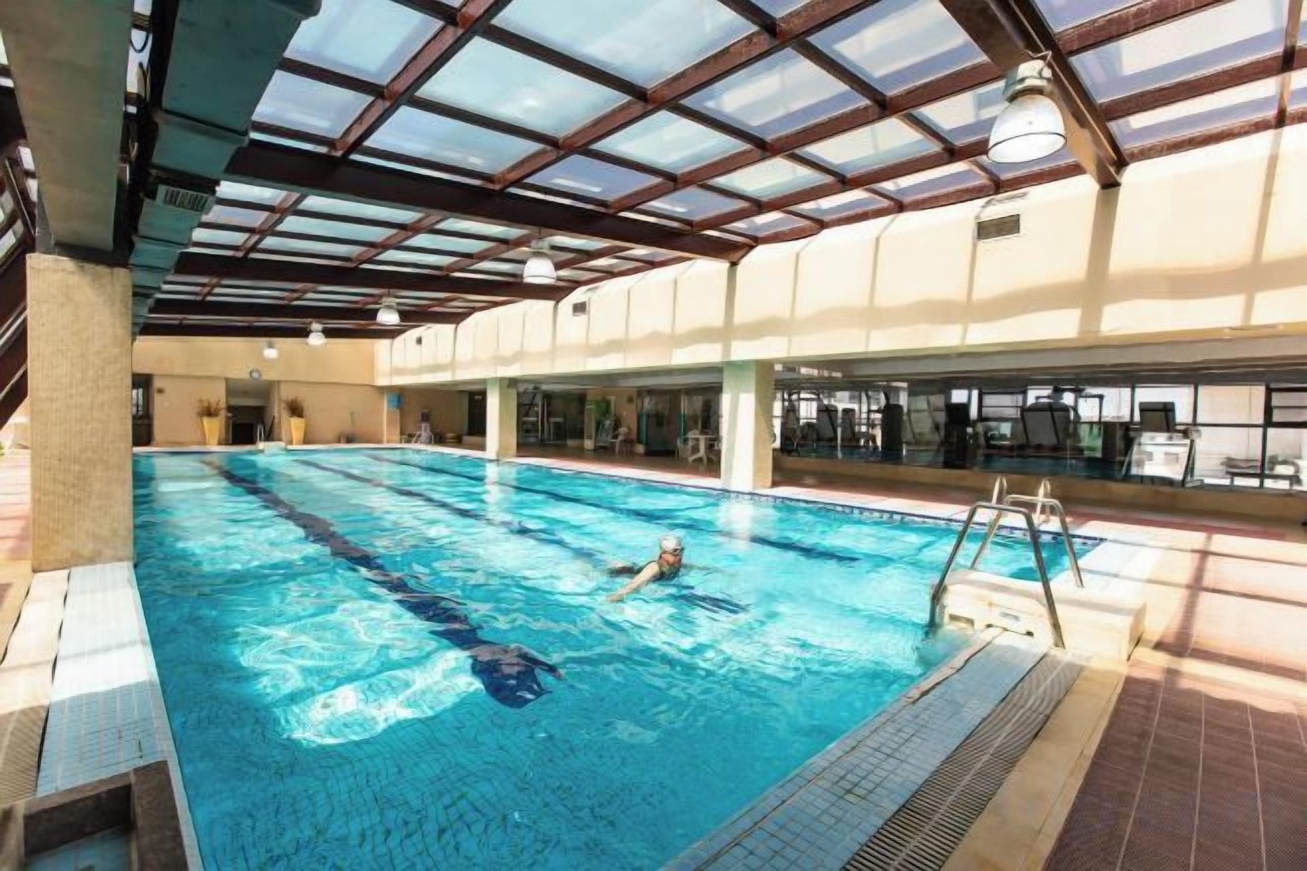 An indoor swimming pool with clear water, a diving board, and a tiled floor.