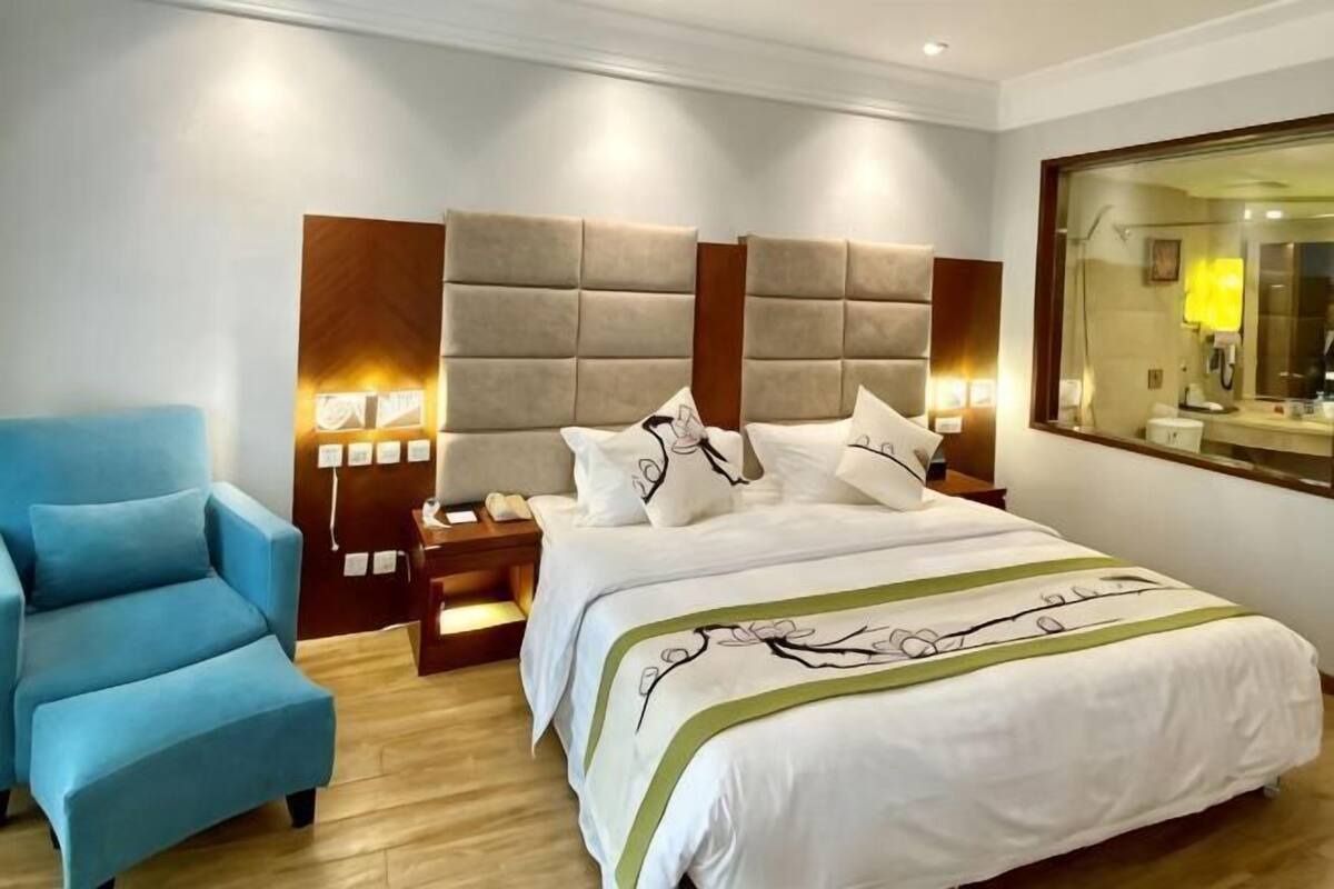 A hotel room with a bed, a blue armchair, bedside tables, and a large mirror.