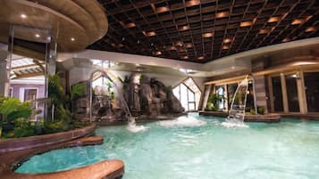 An indoor swimming pool with a waterfall feature, surrounded by tropical plants and a modern ceiling design.