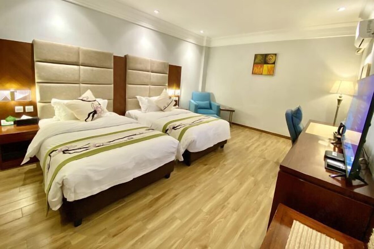 Habitación de hotel con dos camas, un escritorio, una silla y un televisor.