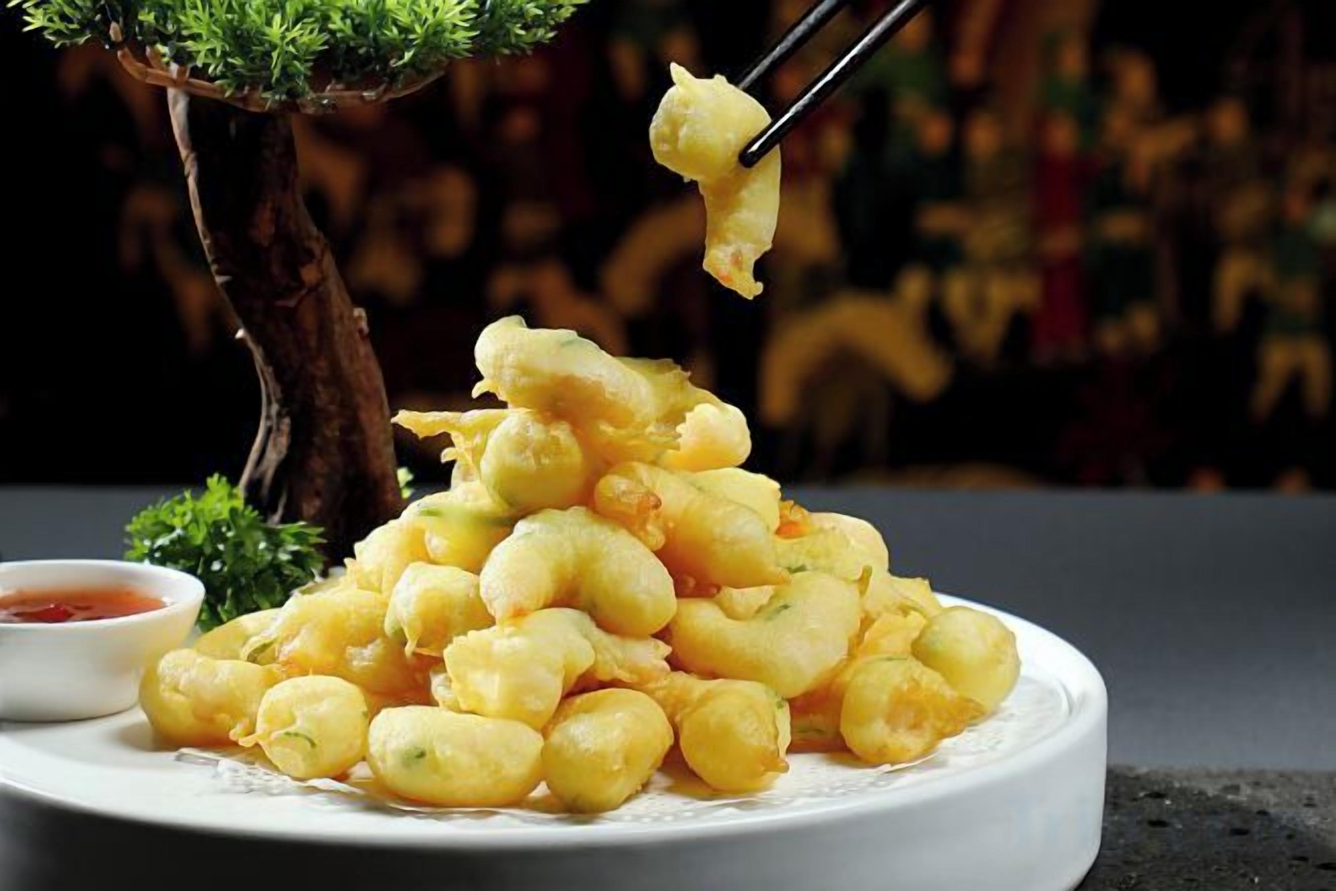 A plate of fried food with a pair of chopsticks lifting a piece, and a small bowl of sauce on the side.