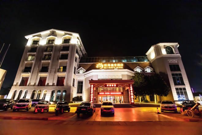 A hotel with a prominent entrance, multiple floors, and a parking area with several cars.
