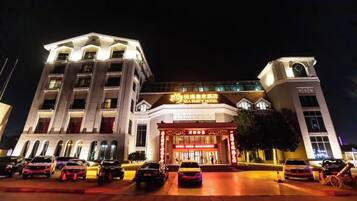 A hotel with a prominent entrance, multiple floors, and a parking area with several cars.