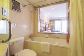 Un baño con bañera, inodoro y ventana con vista a una habitación de hotel.