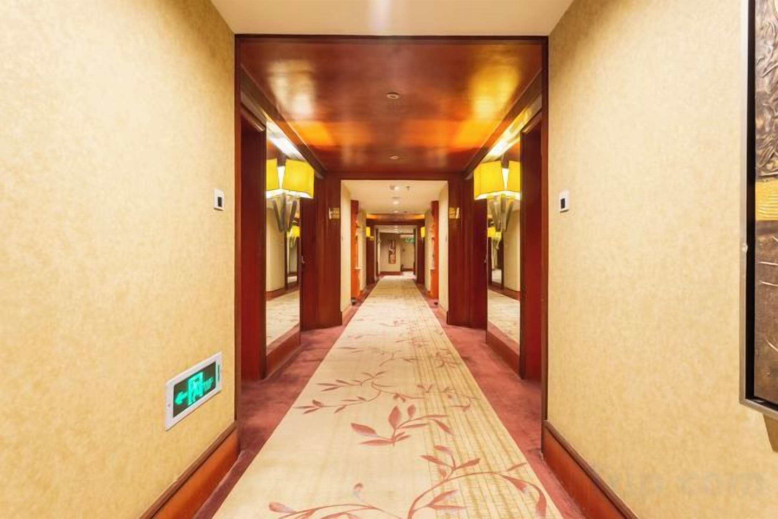 A hotel hallway with a carpeted floor, wooden walls, and wall-mounted lamps.