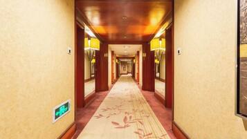 A hotel hallway with a carpeted floor, wooden walls, and wall-mounted lamps.