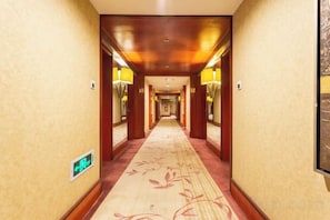 A hotel hallway with a carpeted floor, wooden walls, and wall-mounted lamps. - Sea Party Hotel (Laixi)