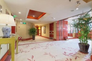 En hotellobby med ett heltäckningsmatta på golvet, en krukväxt, en lampa och en dörr med en skylt.