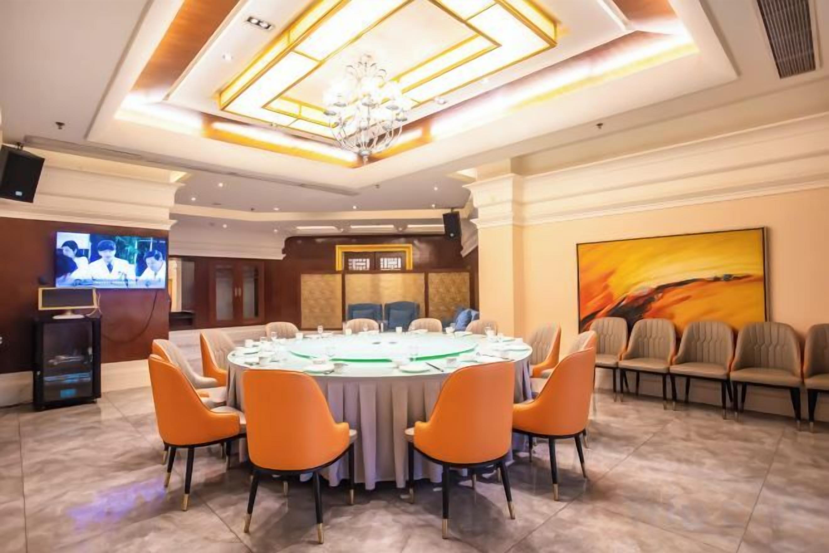 A conference room with a round table, chairs, a chandelier, a TV, and a painting on the wall.