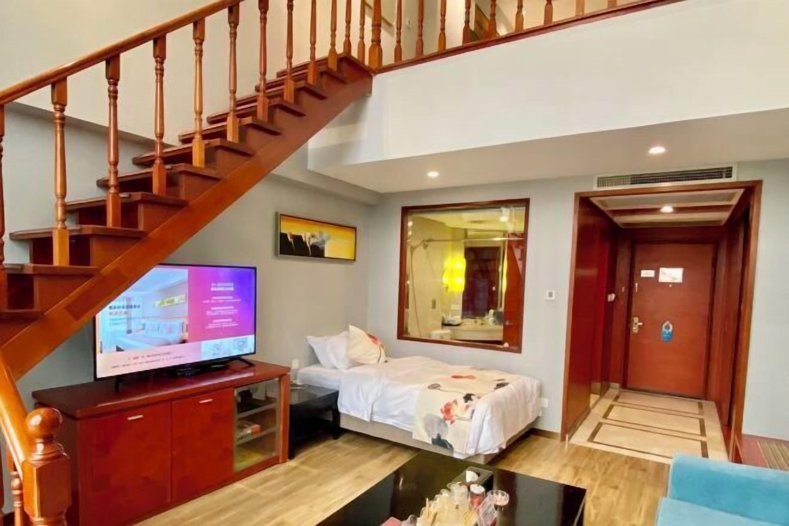 A hotel room with a wooden staircase, a bed, a television, and a mirror.