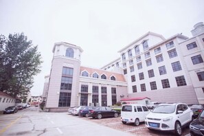 A multi-story building with a central tower, parking lot, and several parked cars. - Sea Party Hotel (Laixi)