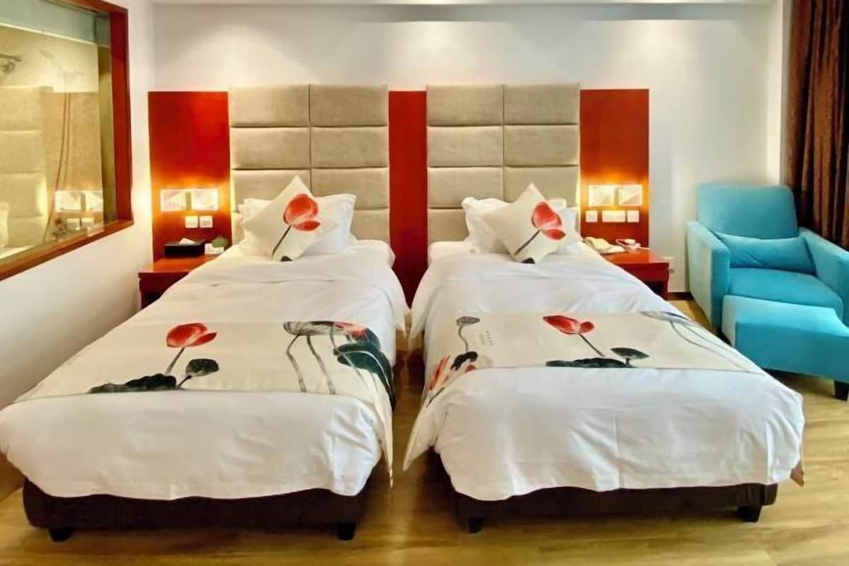 A hotel room with two beds, each with a headboard and bedside lamps. There is a blue armchair and a wooden floor.