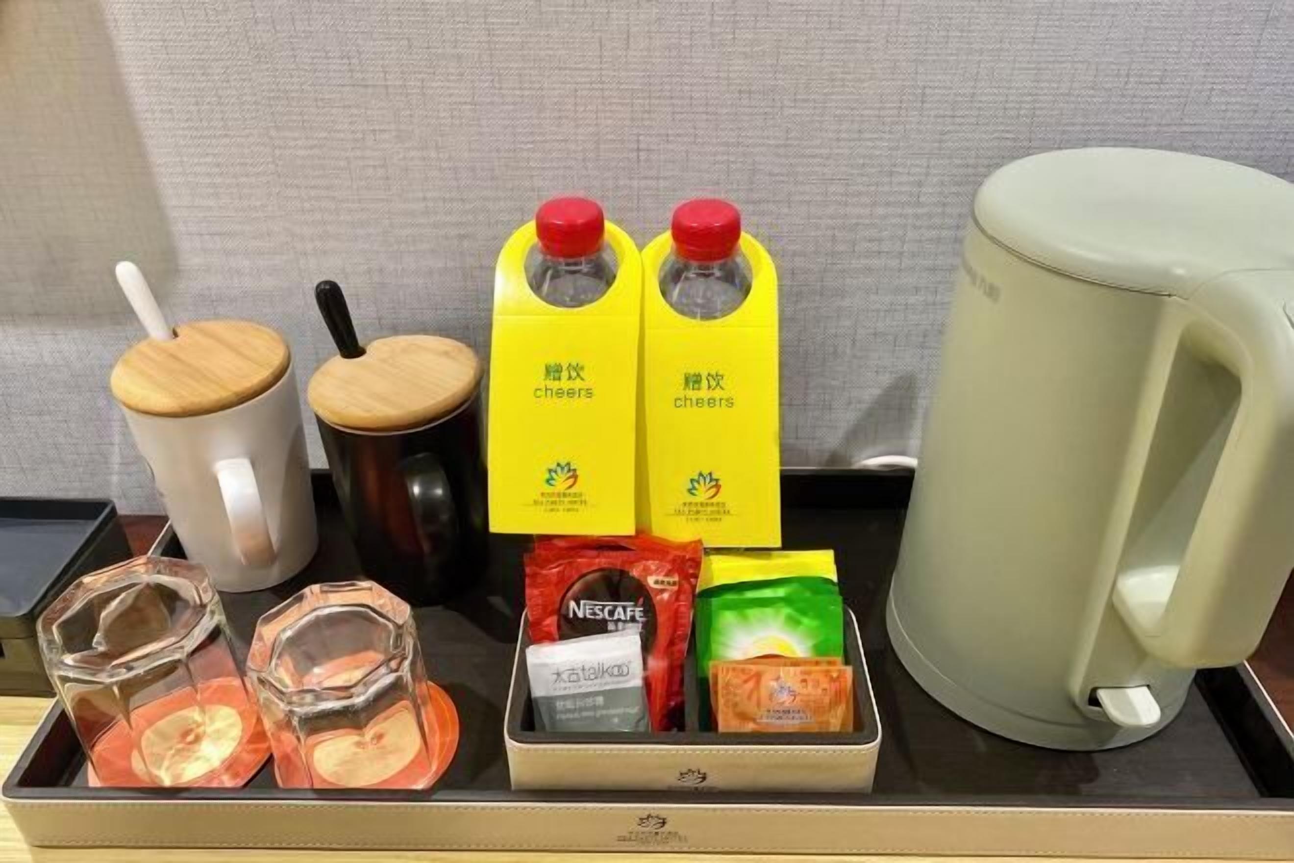 Una bandeja con una taza blanca, dos tazas de madera, dos cartones de jugo amarillo, un paquete verde, un paquete de Nescafé y dos vasos transparentes con líquido anaranjado.