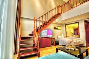 Una sala de estar con una escalera de madera, un televisor de pantalla plana, una cama con ropa de cama blanca y una mesa de centro.