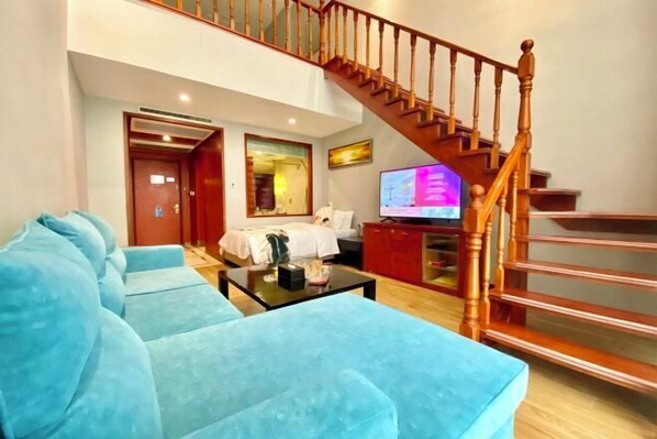 Una sala de estar con un sofá azul, una escalera de madera, un televisor y un mueble rojo.