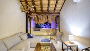 A modern living room with a thatched ceiling, a sofa, a coffee table, and a view of a pool area. - Eco-chic Design Condos Wrapped in Nature's Elements (Tulum)