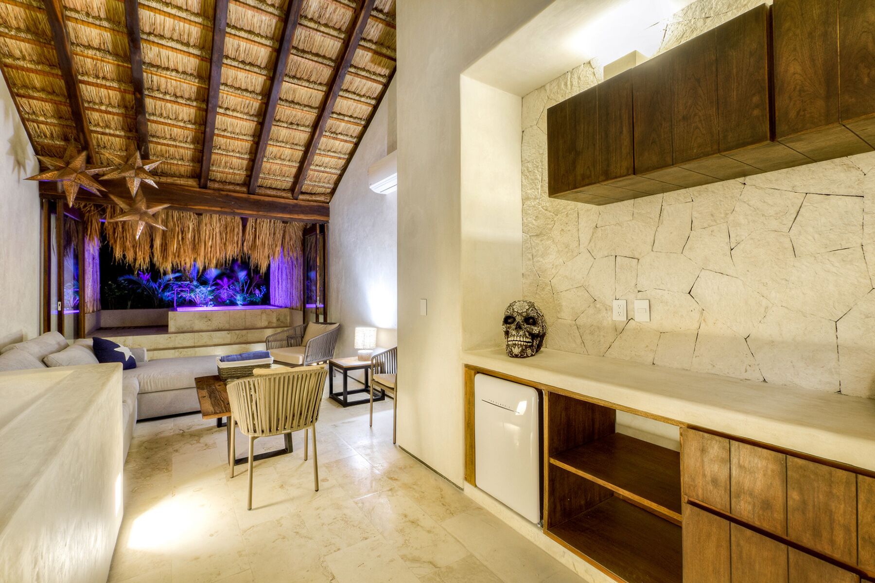 A modern interior with a thatched ceiling, a stone wall, and a minimalist design.