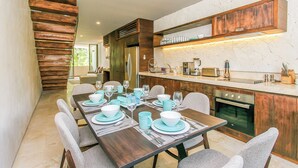 A modern kitchen with wooden cabinets, a built-in oven, and a dining area set for six with a long table and six chairs. - Eco-chic Design Condos Wrapped in Nature's Elements (Tulum)