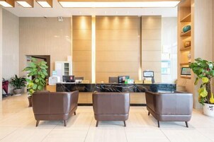 Zona de recepción con mostrador, dos sillones de cuero marrón y una planta en maceta.