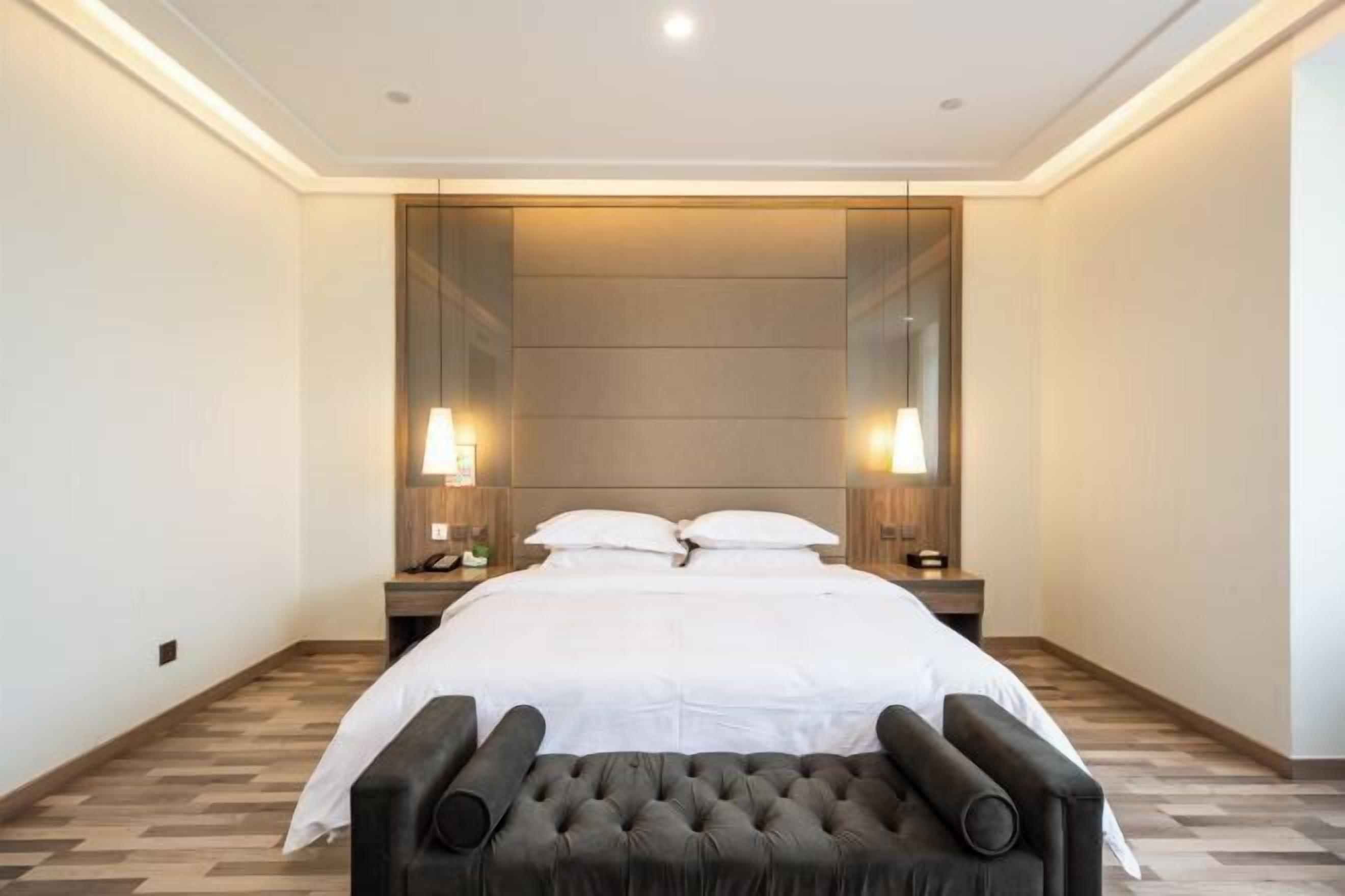Ein Hotelzimmer mit einem großen Bett, zwei Nachttischen, einem Spiegel und einem gepolsterten Kopfteil.