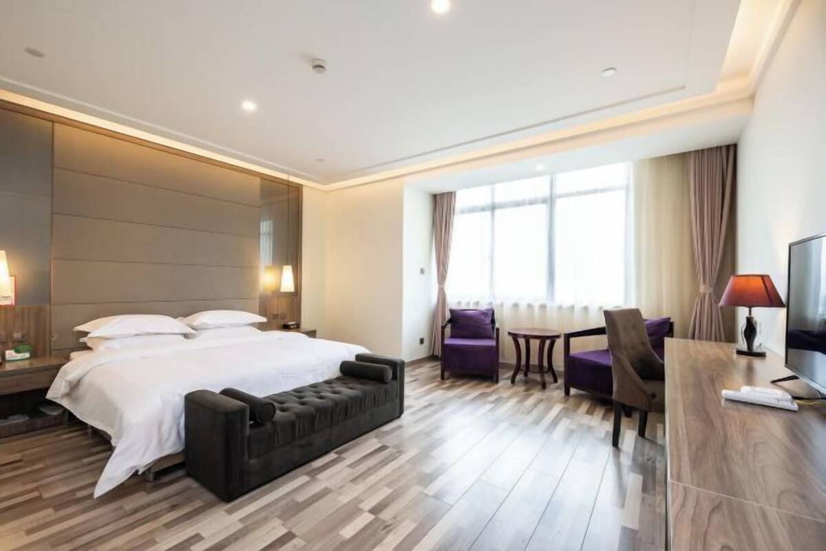 A hotel room with a bed, a seating area with a table and chairs, a television, and a window with curtains.