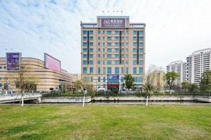 Un hotel de varios pisos con fachada plana, entrada central y un área verde circundante.