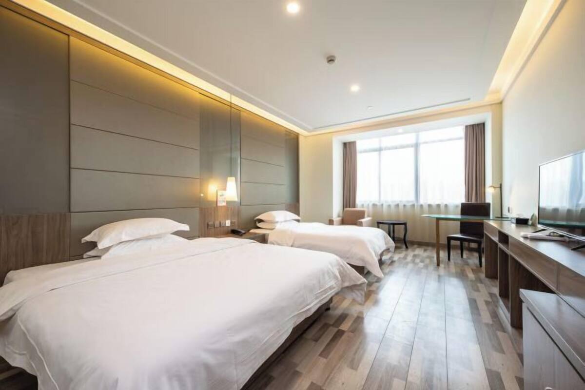 A hotel room with two beds, a desk, a chair, and a TV.