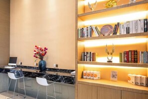 A reception area with a marble counter, two white bar stools, a vase with flowers, and a bookshelf with books and decorative items. - Yasheng Hotel (Taicang Port Area) (Taicang)