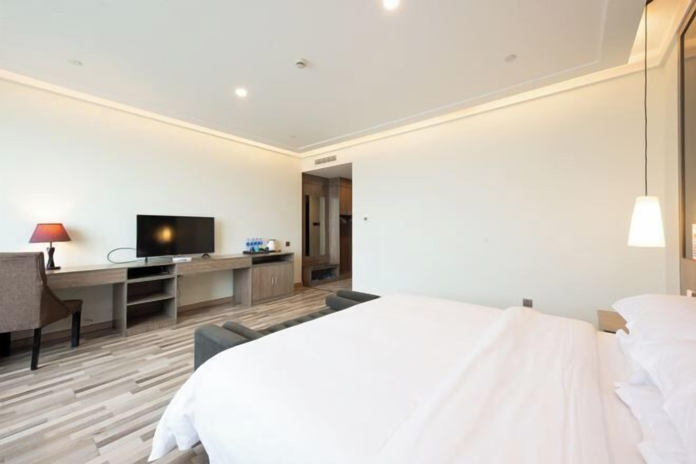 A hotel room with a bed, a desk with a television, a chair, and a lamp.