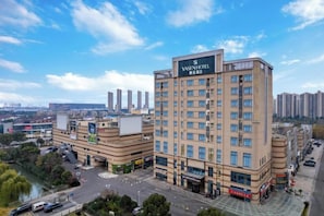 A multi-story hotel with a prominent sign, surrounded by other buildings and a river. - Yasheng Hotel (Taicang Port Area) (Taicang)