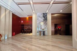 A spacious lobby with a marble floor, a reception desk, and a wall with a decorative pattern. - Fulijin Hotel (Foshan)