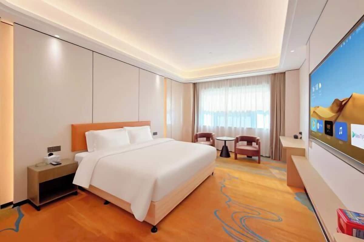 A hotel room with a large bed, a desk, a chair, a TV, and a window with curtains.