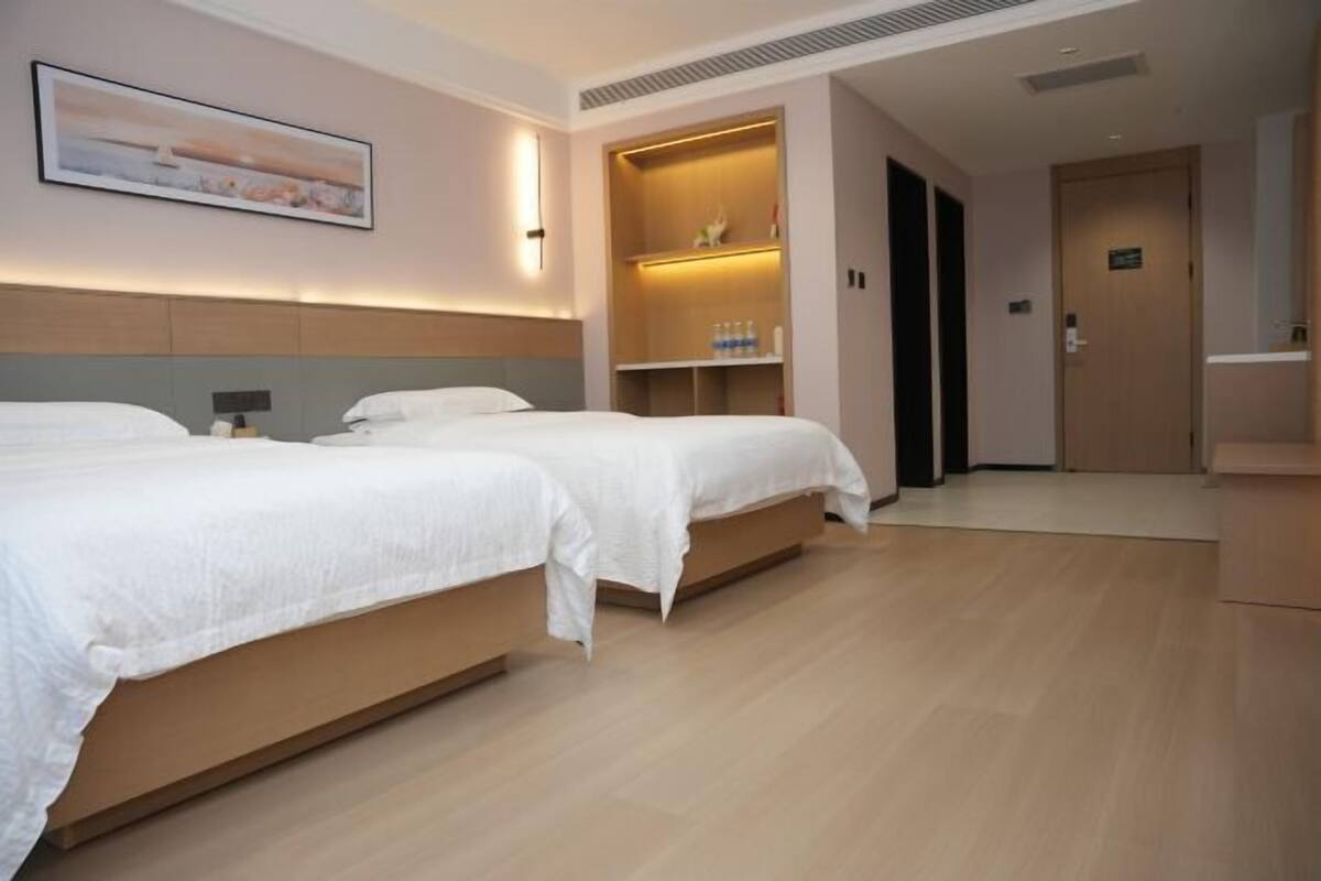 A hotel room with two beds, a built-in shelf with toiletries, and a painting on the wall.